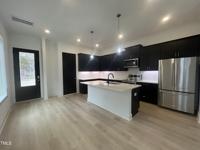 kitchen featuring appliances with stainless steel finishes, an island with sink, light hardwood / wood-style floors, sink, and hanging light fixtures