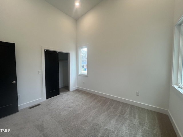 unfurnished bedroom with high vaulted ceiling, a closet, and light carpet