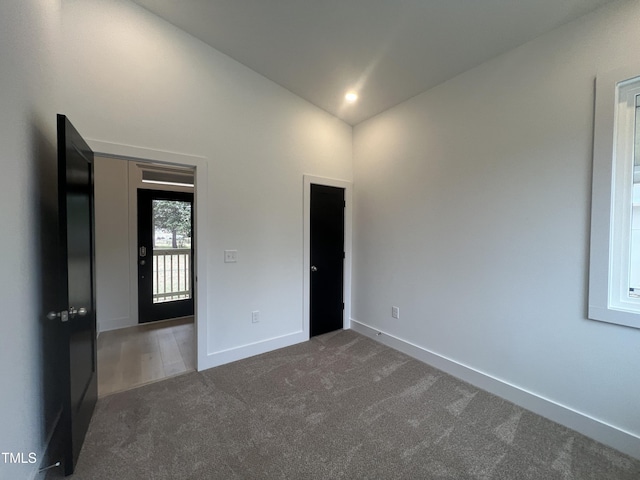 unfurnished room with dark colored carpet and lofted ceiling