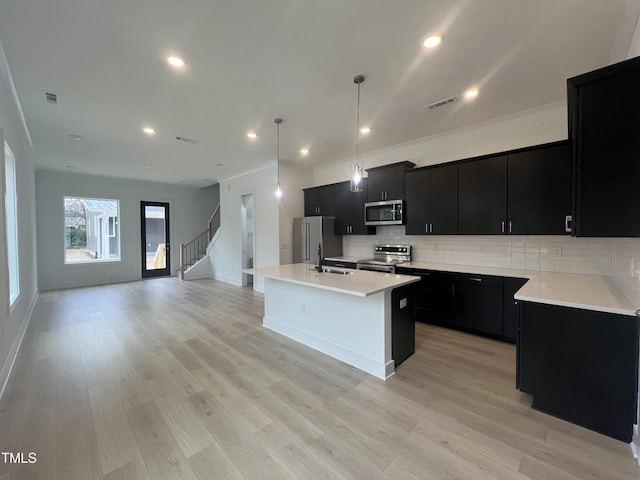 kitchen with hanging light fixtures, sink, light hardwood / wood-style flooring, stainless steel appliances, and a center island with sink