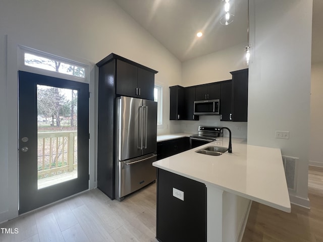 kitchen featuring appliances with stainless steel finishes, sink, high vaulted ceiling, kitchen peninsula, and light hardwood / wood-style flooring