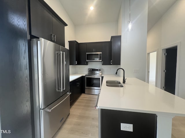 kitchen with stainless steel appliances, sink, hanging light fixtures, kitchen peninsula, and light wood-type flooring