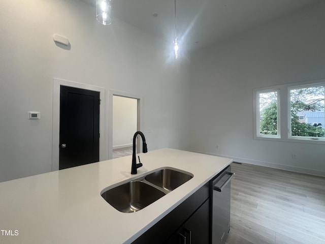 kitchen with a high ceiling, dishwasher, light hardwood / wood-style floors, sink, and hanging light fixtures