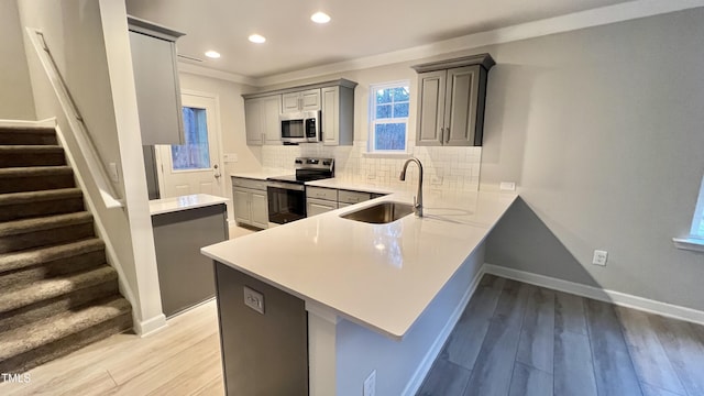 kitchen with kitchen peninsula, appliances with stainless steel finishes, sink, light hardwood / wood-style flooring, and gray cabinets