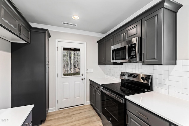 kitchen featuring light wood-style flooring, stainless steel appliances, visible vents, light countertops, and decorative backsplash