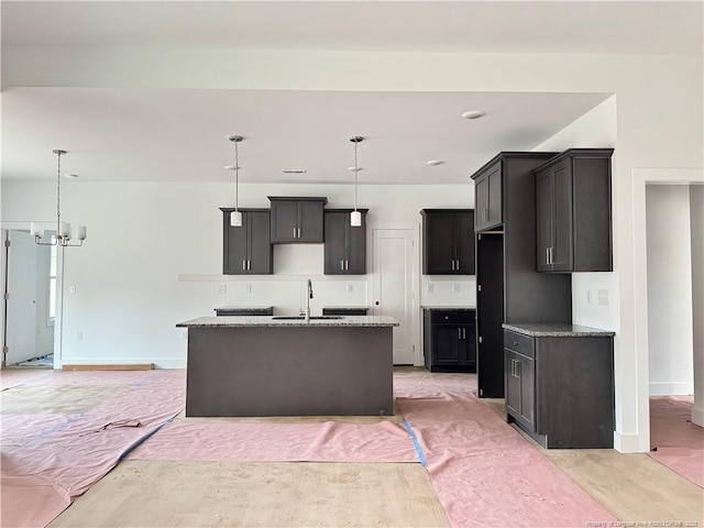 kitchen featuring baseboards, light wood-style flooring, a kitchen island with sink, and a sink