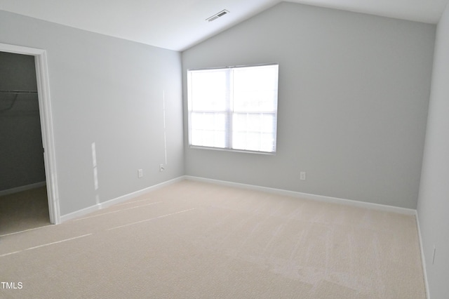 unfurnished bedroom with a walk in closet, a closet, light colored carpet, and vaulted ceiling