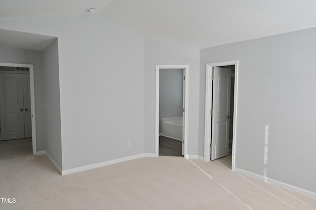 unfurnished bedroom featuring connected bathroom, light carpet, and lofted ceiling