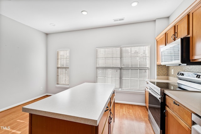 kitchen featuring light wood-type flooring, decorative backsplash, electric range, and a center island