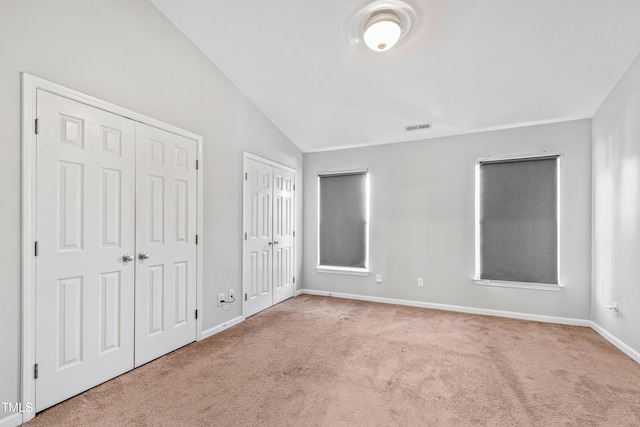 unfurnished bedroom featuring light colored carpet, vaulted ceiling, and multiple closets