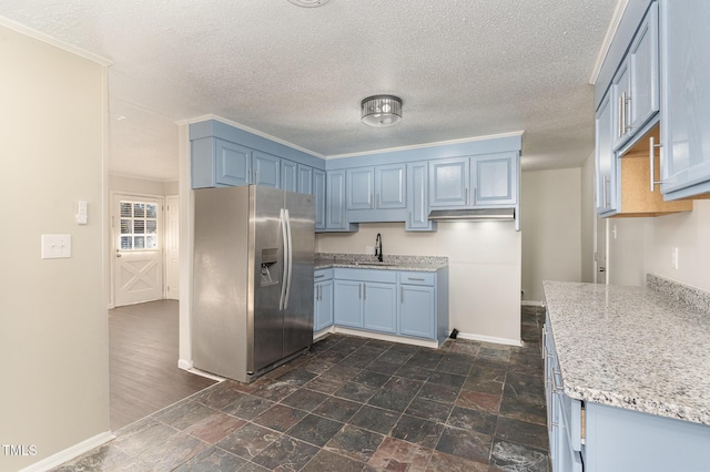 kitchen featuring blue cabinetry, stainless steel fridge, light stone counters, and a textured ceiling