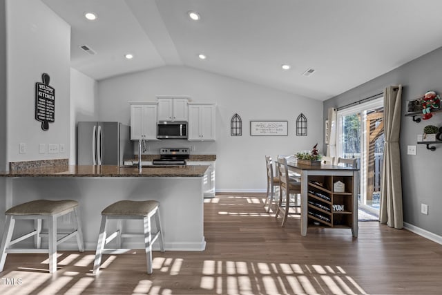 kitchen with white cabinets, vaulted ceiling, dark hardwood / wood-style flooring, kitchen peninsula, and stainless steel appliances