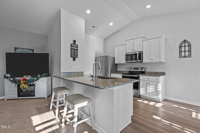 kitchen featuring a kitchen bar, appliances with stainless steel finishes, kitchen peninsula, vaulted ceiling, and white cabinets