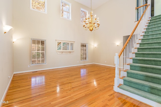 unfurnished living room with a notable chandelier, wood-type flooring, and a high ceiling