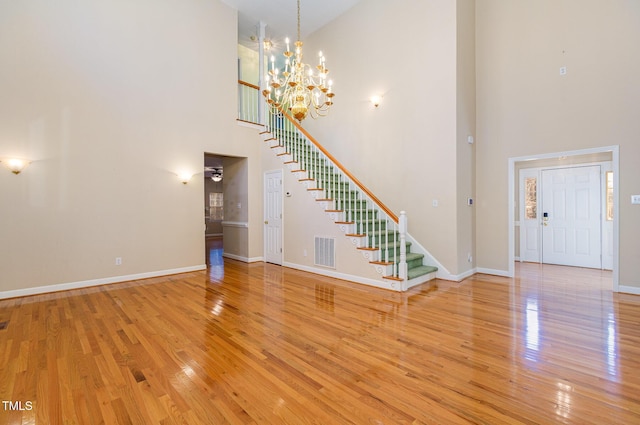 unfurnished living room with a towering ceiling, a notable chandelier, and light wood-type flooring