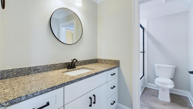 bathroom featuring baseboards, toilet, shower / bath combination with glass door, wood finished floors, and vanity