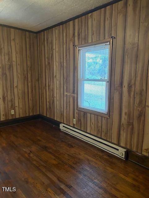 empty room featuring dark hardwood / wood-style floors, a textured ceiling, wooden walls, and a baseboard radiator