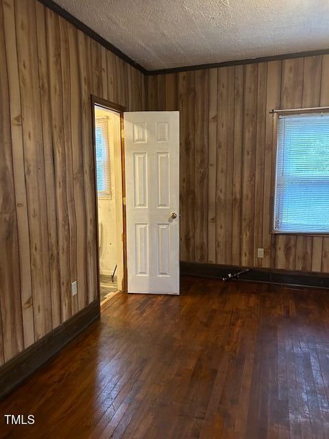 spare room with a textured ceiling, wooden walls, and dark hardwood / wood-style floors