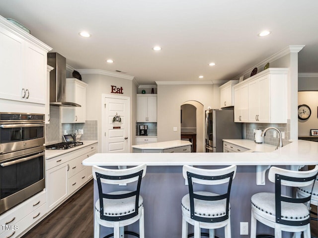 kitchen with wall chimney exhaust hood, dark hardwood / wood-style floors, appliances with stainless steel finishes, tasteful backsplash, and white cabinetry