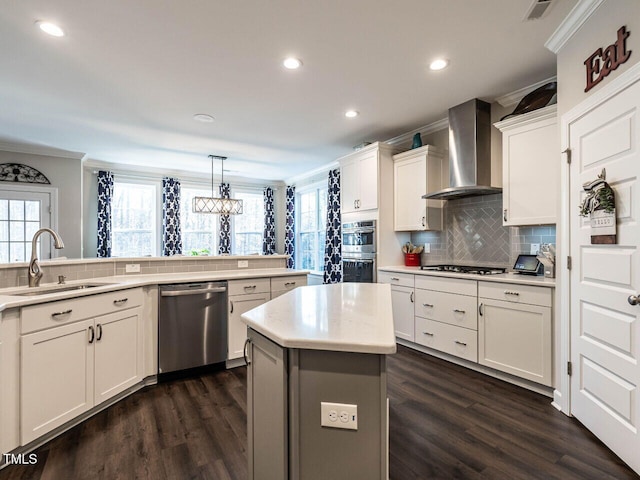 kitchen with stainless steel appliances, sink, wall chimney range hood, white cabinets, and a center island