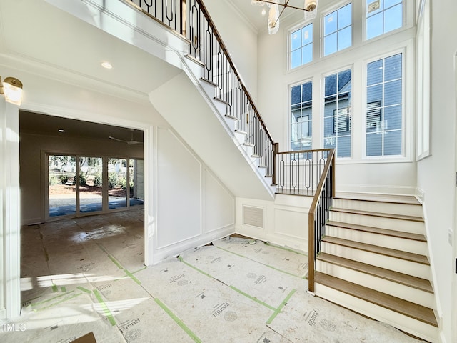 stairs with an inviting chandelier, a high ceiling, ornamental molding, and a decorative wall