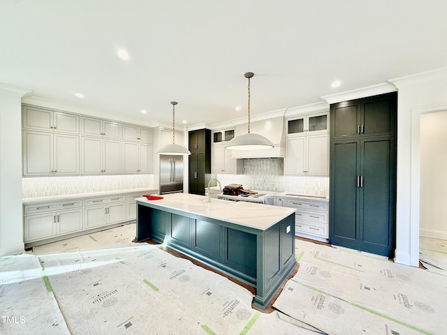 kitchen featuring hanging light fixtures, a large island with sink, backsplash, stainless steel built in fridge, and crown molding