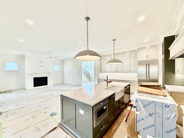 kitchen with an island with sink, white cabinetry, built in appliances, light stone countertops, and pendant lighting