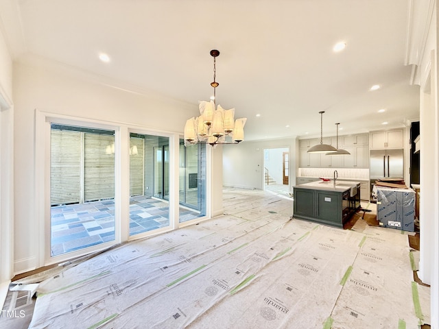 kitchen featuring an island with sink, a chandelier, pendant lighting, crown molding, and backsplash