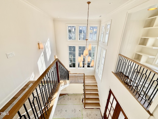 staircase with a chandelier, crown molding, and built in shelves