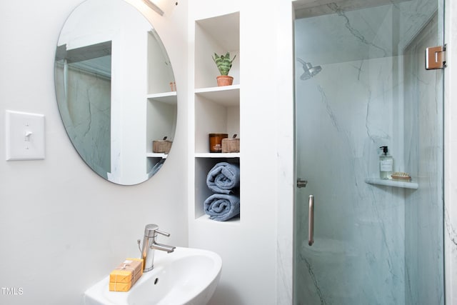 bathroom featuring a shower with shower door, built in features, and sink