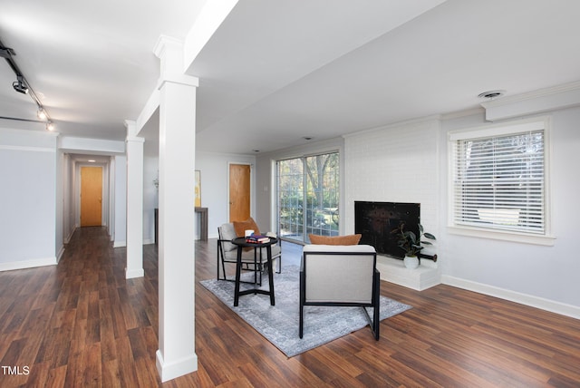 living room featuring track lighting, crown molding, dark hardwood / wood-style floors, ornate columns, and a fireplace