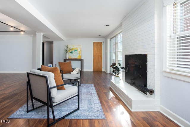 living room featuring a healthy amount of sunlight, dark hardwood / wood-style flooring, a fireplace, and decorative columns