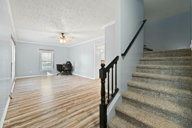 stairs with ceiling fan, wood-type flooring, a textured ceiling, and ornamental molding