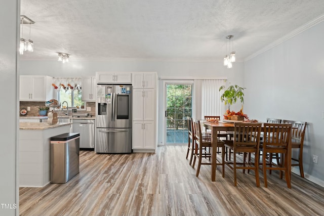 kitchen with a wealth of natural light, white cabinetry, pendant lighting, and stainless steel appliances