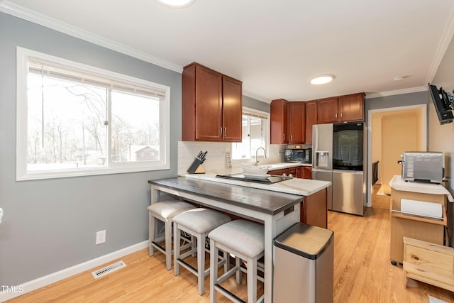 kitchen with black appliances, plenty of natural light, light hardwood / wood-style floors, and a breakfast bar area