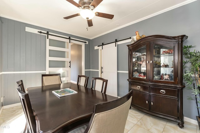 tiled dining space featuring a barn door, wooden walls, ceiling fan, and crown molding