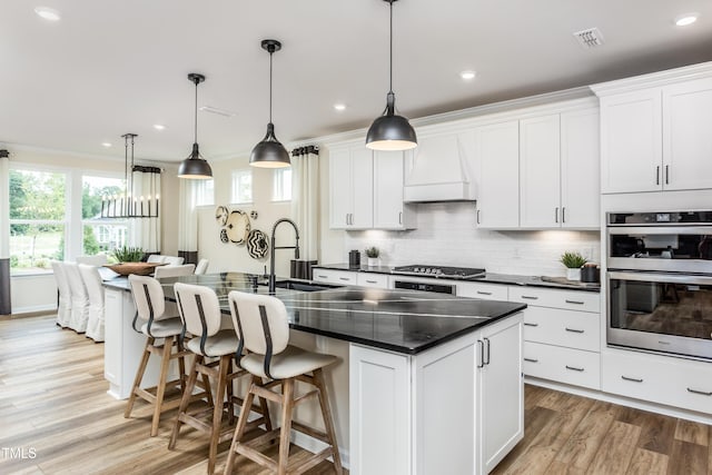 kitchen featuring dark countertops, custom range hood, decorative backsplash, appliances with stainless steel finishes, and a sink