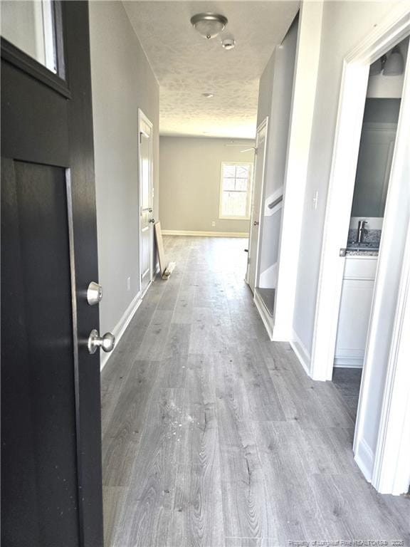 corridor with a sink, a textured ceiling, baseboards, and wood finished floors