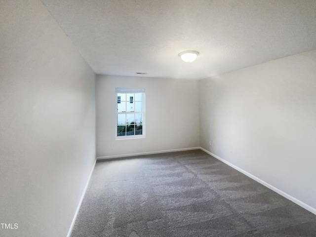 spare room with a textured ceiling and dark colored carpet