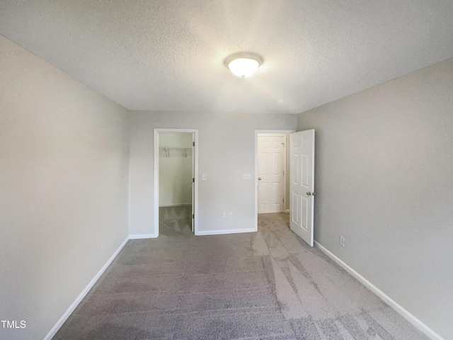 unfurnished bedroom with carpet, a spacious closet, a textured ceiling, and a closet