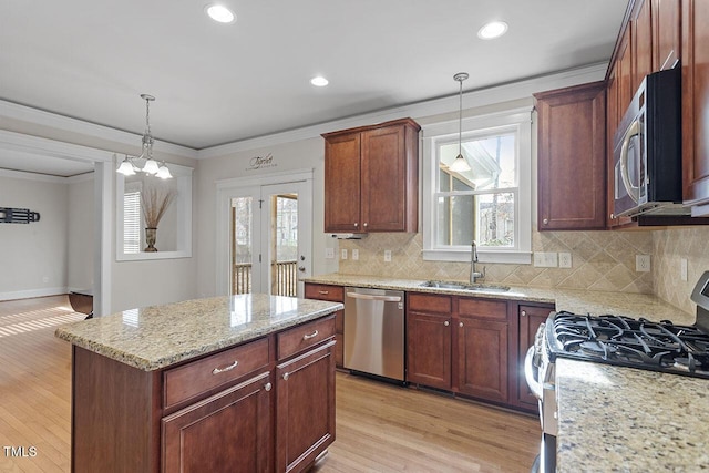 kitchen with light stone counters, light wood-style flooring, stainless steel appliances, a sink, and crown molding