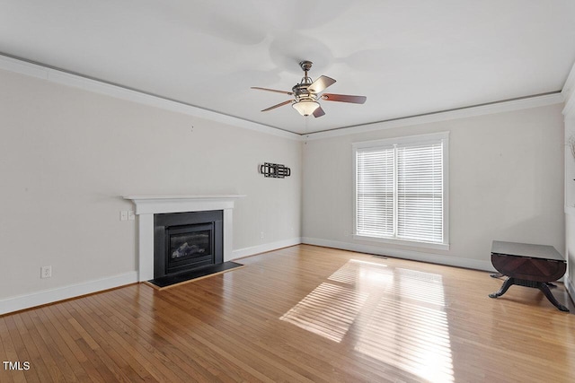 unfurnished living room featuring ornamental molding, a glass covered fireplace, a ceiling fan, and light wood-style floors