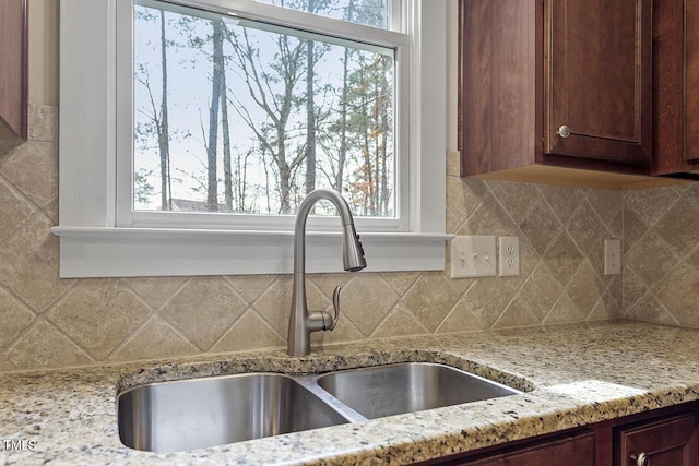 kitchen with decorative backsplash, a sink, and light stone countertops