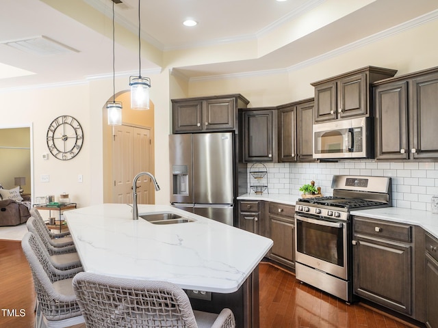 kitchen with a kitchen bar, stainless steel appliances, dark wood-type flooring, sink, and an island with sink