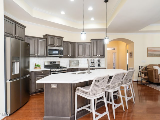 kitchen with stainless steel appliances, a kitchen island with sink, sink, dark hardwood / wood-style floors, and hanging light fixtures