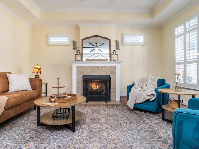 living room featuring a raised ceiling, a tile fireplace, and crown molding