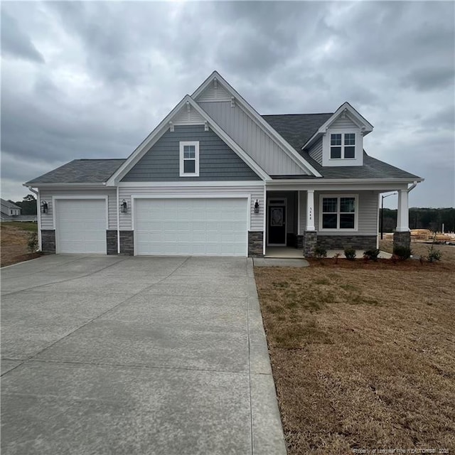 craftsman-style house featuring driveway, a front yard, stone siding, an attached garage, and a porch