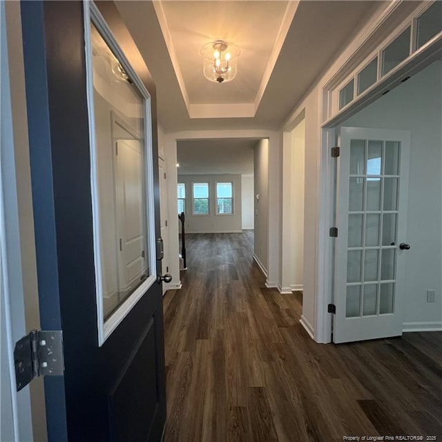hallway with baseboards, a raised ceiling, dark wood-type flooring, and a chandelier