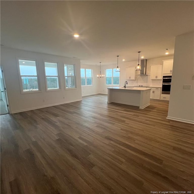 unfurnished living room featuring recessed lighting, an inviting chandelier, baseboards, dark wood finished floors, and a sink