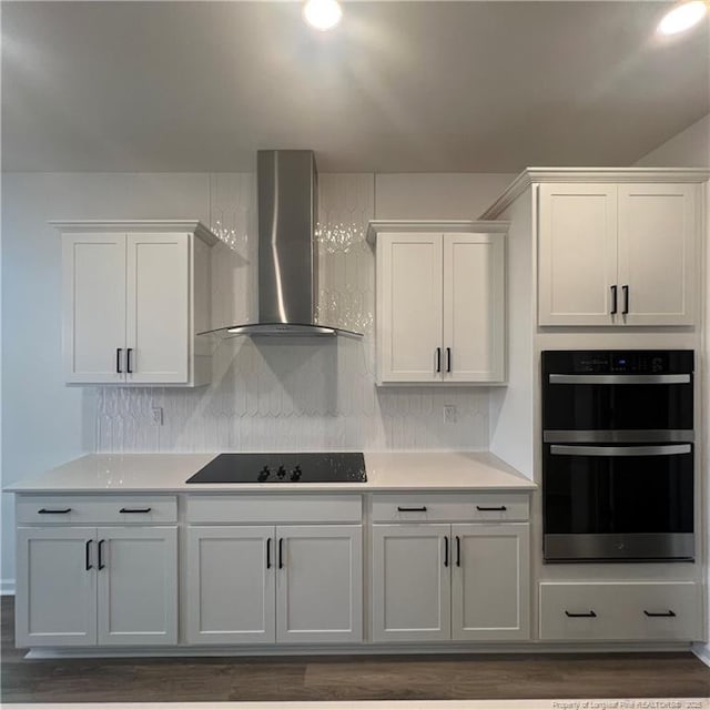 kitchen with light countertops, double oven, wall chimney exhaust hood, tasteful backsplash, and black electric stovetop